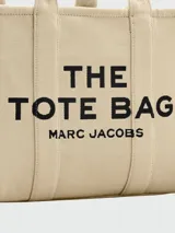 Bolso tote grande Marc Jacobs color beige con estampado del logo de la marca en negro. Tiene doble asa de mano y laterales con inscripción de la marca.