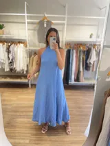 Vestido largo confeccionado en lino de color celeste, con cuello halter y silueta holgada de corte evasé.