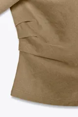 Camiseta color marrón con cuello redondo, manga sisa caída en un lado y manga corta en el otro. Tiene detalle de frunces laterales.