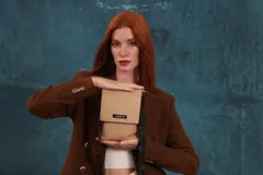 Bandolera tipo phone bag pequeña, color marrón claro, con correa de galón regulable. Tiene un compartimento principal y un bolsillo adicional con tapa.