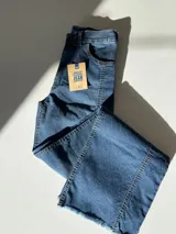 Pantalón de jean de tiro alto, corte flare, color azul oscuro, con costuras frontales y detalle desflecado en el ruedo.