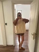 Buzo beige con mangas marrones y cuello lila, de corte holgado y largo a la cadera.