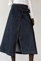 Falda midi de denim azul oscuro, de tiro alto, con diseño cruzado, abertura frontal y ajuste lateral con doble hebilla metálica.