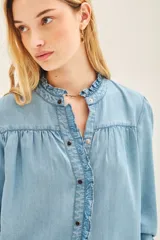 Camisa celeste de tencel con calce recto, cuello redondo con volados, canesú en delantero y espalda, y mangas largas terminadas en puño con botón snap.