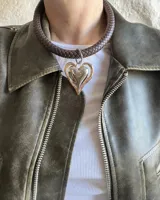 Collar con cordón trenzado de cuero sintético color negro, con dije circular plateado con centro de piedra blanca con pintitas negras. Cierre con mosquetón plateado.