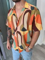 Camisa de hombre de manga corta con cuello clásico y cierre abotonado. Presenta un estampado abstracto con formas geométricas en tonos naranja, marrón, verde, beige y rosa.