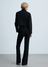 Chaqueta corta negra de corte recto con cuello camisero, manga larga, dos bolsillos de parche delanteros, cierre frontal con botones ocultos y forro interior.