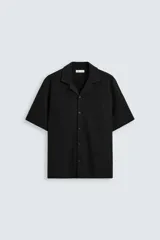 Camisa negra de manga corta con cuello bowling y cierre frontal con botones.