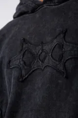 Buzo canguro negro con capucha, calce oversize, confeccionado en frisa 100% algodón con lavado gastado y aplique cosido en el pecho.