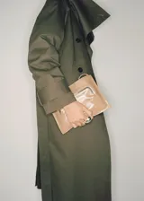 Trench coat verde militar con cuello solapa ancho, doble botonadura, cinturón desmontable, trabillas en cintura y puños, dos bolsillos laterales y forro interior.