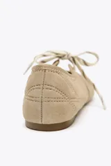 Zapato plano tipo bailarina color beige, de serraje, con puntera redondeada, suela plana y cierre con cordones.