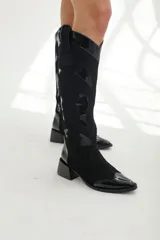 Bota bucanera negra de cuero, con detalles en charol y gamuza, diseño estilo western con punta fina y taco bajo.