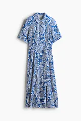 Vestido midi camisero con estampado de hojas blancas sobre fondo azul. Tiene cuello camisero, botonadura frontal, mangas cortas raglán, elástico en la cintura y cinturón extraíble para atar.