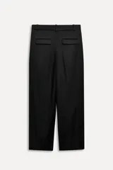 Pantalón negro de tiro alto con trabillas, bolsillos laterales y falsos bolsillos de vivo con solapa en la espalda. Detalle de cinturilla interior a contraste con pespuntes. Pinzas en el delantero. Cierre frontal con cremallera, botón interior y gancho metálico.
