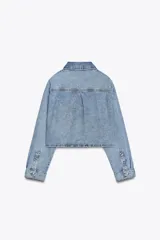 Camisa corta de denim celeste, con cuello solapa, manga larga, bolsillo delantero de plastrón y cierre frontal con botones metálicos.