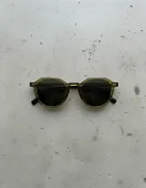 Lentes de sol unisex de forma geométrica, con armazón color mostaza oscuro y lentes polarizadas color negro.