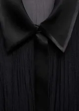 Camisa negra semitransparente de tejido fluido con ribetes satinados, cuello camisero, cierre de botones y mangas largas abotonadas.