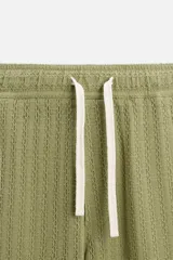 Pantalón verde oliva de corte relaxed fit, confeccionado en tejido de algodón con textura. Tiene cintura elástica ajustable con cordón, bolsillos frontales y un bolsillo trasero de parche.