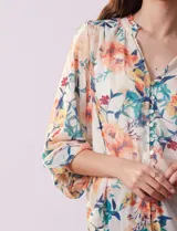 Blusa de gasa estampada con flores, cuello a la base con detalle plisado y escote en V. Apertura central con botones de nácar y mangas largas con terminación fruncida. Incluye musculosa interna.