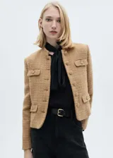 Chaqueta corta color beige de tweed con cuello mao, cierre frontal con botones y cuatro bolsillos delanteros con solapa.