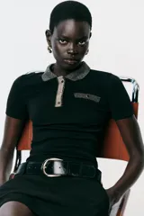 Chomba negra de corte slim fit, con cuello polo y mangas cortas. Presenta un falso bolsillo en el pecho y cierre frontal con botones. Detalle de hilo metalizado en cuello, bolsillo y tapeta.