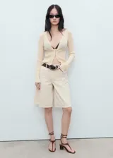 Cardigan de punto fino color crema, con escote en V y cierre frontal de botones. Presenta ribetes en contraste en los puños y un tejido semitransparente.