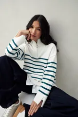 Polera blanca de punto con cuello alto y cierre metálico, de calce relajado y diseño a rayas horizontales azules.
