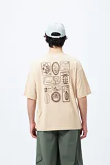 Remera color beige de corte amplio con mangas cortas y estampado de una postal con una palmera en el pecho.