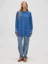 Sweater color crema con tejido en ochos, cuello redondo, puños acanalados con doble raya azul y tajos a los costados.