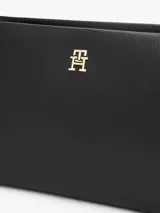 Cartera bandolera negra con textura granulada, correa ajustable y logo metálico dorado de Tommy Hilfiger en el frente.