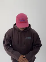 Gorro tipo gorra color fucsia con visera, y estampado frontal en azul con la palabra "attitude" y otros textos.