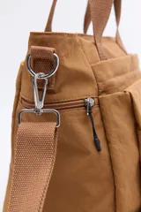 Cartera de nylon color verde militar con asas superiores reforzadas y correa larga regulable y desmontable. Cuenta con bolsillos frontales y laterales con cierre metálico, y un logo de la marca en la parte inferior central.