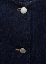 Chaqueta corta de jean azul oscuro, con cuello redondo, cierre frontal con botones y dos bolsillos de parche en la parte delantera.