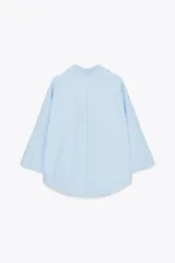 Camisa marrón de popelina con cuello solapa, escote en pico, cierre frontal con botones y mangas anchas con puños.