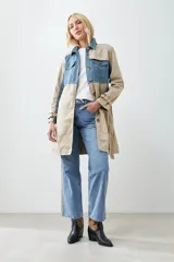 Trench largo color beige con secciones en denim azul, cuello camisero, cierre frontal con botones y bolsillos con solapa en el pecho.