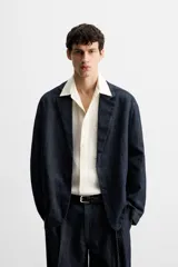 Blazer azul oscuro de denim, corte relaxed fit, con cuello de solapas de muesca, manga larga con puños abotonados, bolsillos de solapa en la cadera, abertura en el centro de la espalda y cierre frontal con botones. Sin forro interior.
