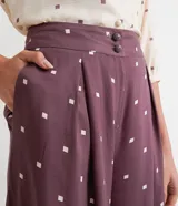 Pantalón pantacourt de viscosa color lila con estampado de pequeños cuadrados blancos. Tiene pinzas delanteras, bolsillos laterales y cierre con botones.