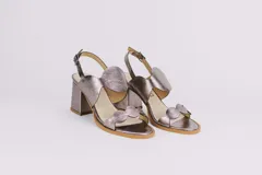 Sandalias plateadas de cuero con taco ancho y diseño de ondas en el empeine. Cierre con hebilla en el tobillo.