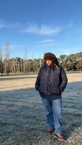 Campera puffer negra con estampado de flores y aves, capucha con borde de piel sintética marrón, bolsillos laterales y forro de algodón.