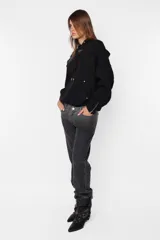 Buzo hoodie negro de frisa, corte oversize, con puños y cintura de rib al tono, capucha forrada y bolsillo canguro. Detalle de remaches en la boca del bolsillo, cierre metálico niquelado en el puño de las mangas, cordones con ojalillos y punteras personalizadas de marca. Cordones atracados en delantero con bordado de marca.