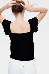 Top corto negro en punto arrugado con escote corazón, manga circular y sección cut-out con cordón para ajustar en el busto. Modelo ajustado sobre el busto con copas preformadas fruncidas y peplum con leve vuelo.