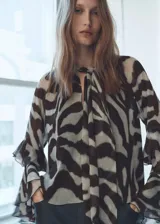Blusa de manga larga acampanada con estampado animal print bicolor. Tiene cuello pico con lazo, detalle de volantes y diseño recto.