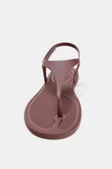 Sandalia plana color marrón con efecto engomado, tira delantera para el dedo, cierre con tira ajustable al tobillo y punta redonda.
