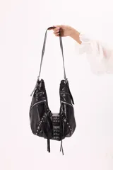 Bolso bandolera negro de símil cuero con múltiples cierres, tachas plateadas y detalle de hebilla tipo cinturón al frente.