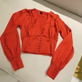 Camisa color beige de satén con escote en V y abotonada al frente, de mangas largas con puños abotonados.