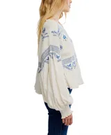 Blusa color crema con bordados azules, mangas largas abullonadas con puños elásticos y cuello redondo con detalle de volados.