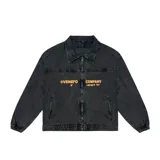 Chaqueta de jean negro con efecto lavado, corte recto, cuello clásico, cierre frontal con cremallera, bolsillos laterales y puños elásticos. Estampado con el texto "VENEFO COMPANY" en color naranja.
