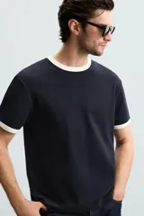 Camiseta azul marino de corte regular, con cuello redondo y mangas cortas. Presenta ribete blanco en cuello y mangas.
