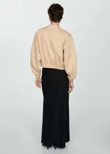 Chaqueta bomber color beige con cierre frontal, cuello redondo, mangas largas con puños elásticos y dos bolsillos delanteros con solapa.