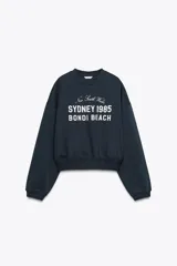 Sudadera azul marino de cuello redondo y manga larga con estampado frontal que dice "New South Wales Sydney 1985 Bondi Beach" en color blanco.